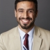 Dr. Ali M. Rahman in a beige blazer and a striped tie, seated in front of a gray background. 