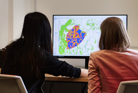 A student and instructor seated at a computer station looking at a computer screen with a digital mapping image. 