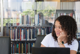 Woman at table in library reading room with laptop in front of her