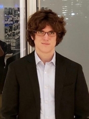 J.D. Porter in a white shirt and dark jacket standing in front of a glass wall. 