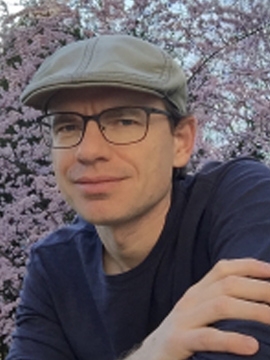 Jared Farmer in a dark shirt and grey cap standing in front of a cherry tree