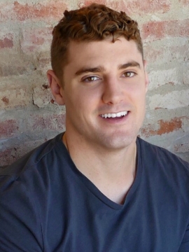 Matt Aiello in a dark t shirt in front of a brick wall